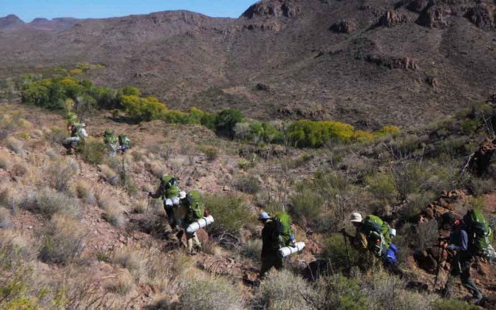 a group of gap year students wearing backpacks hike through a desert landscape on an outward bound semester expedition 